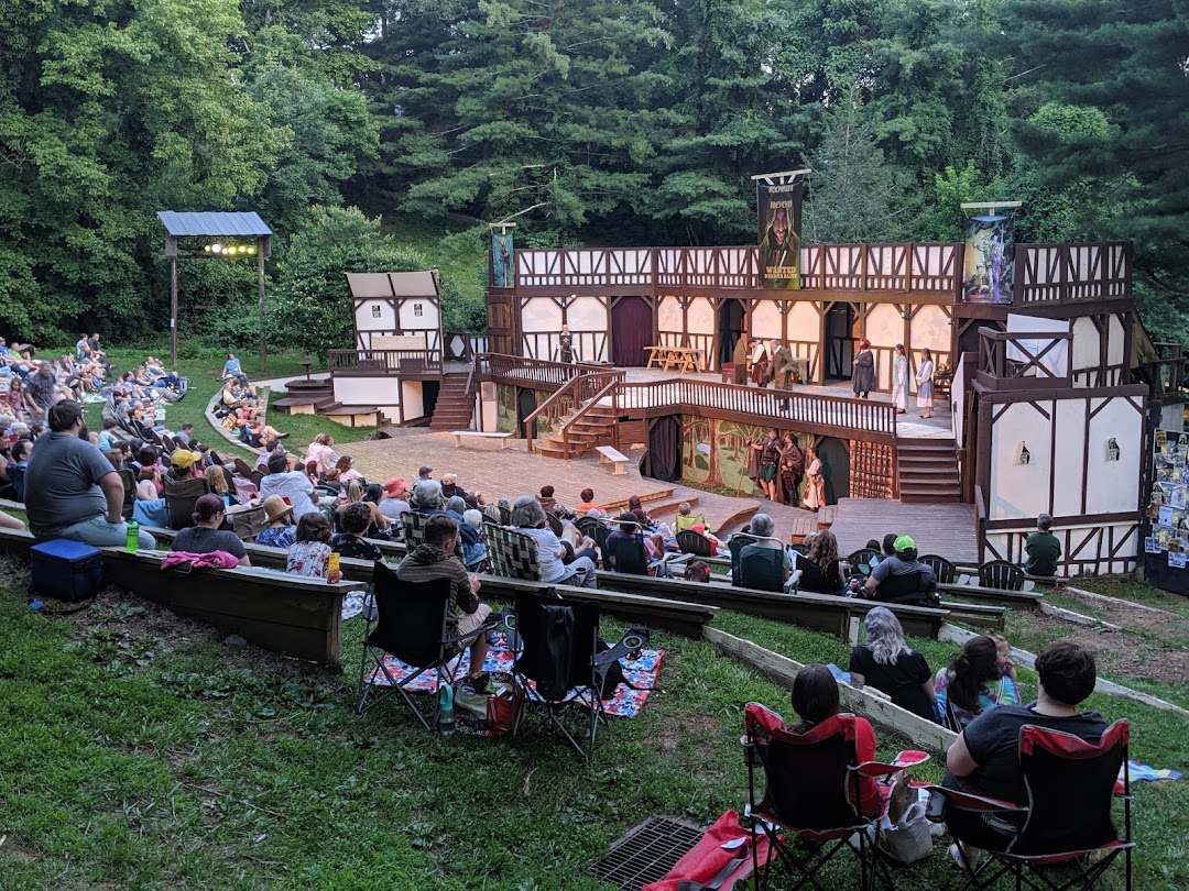 The stage of the Montford Park Players during a performance with audience members sitting on the grassy hill in front of the stage.