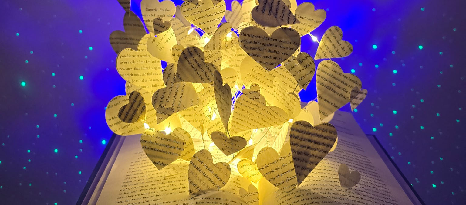 Open book with glowing paper hearts and a starry blue backdrop.