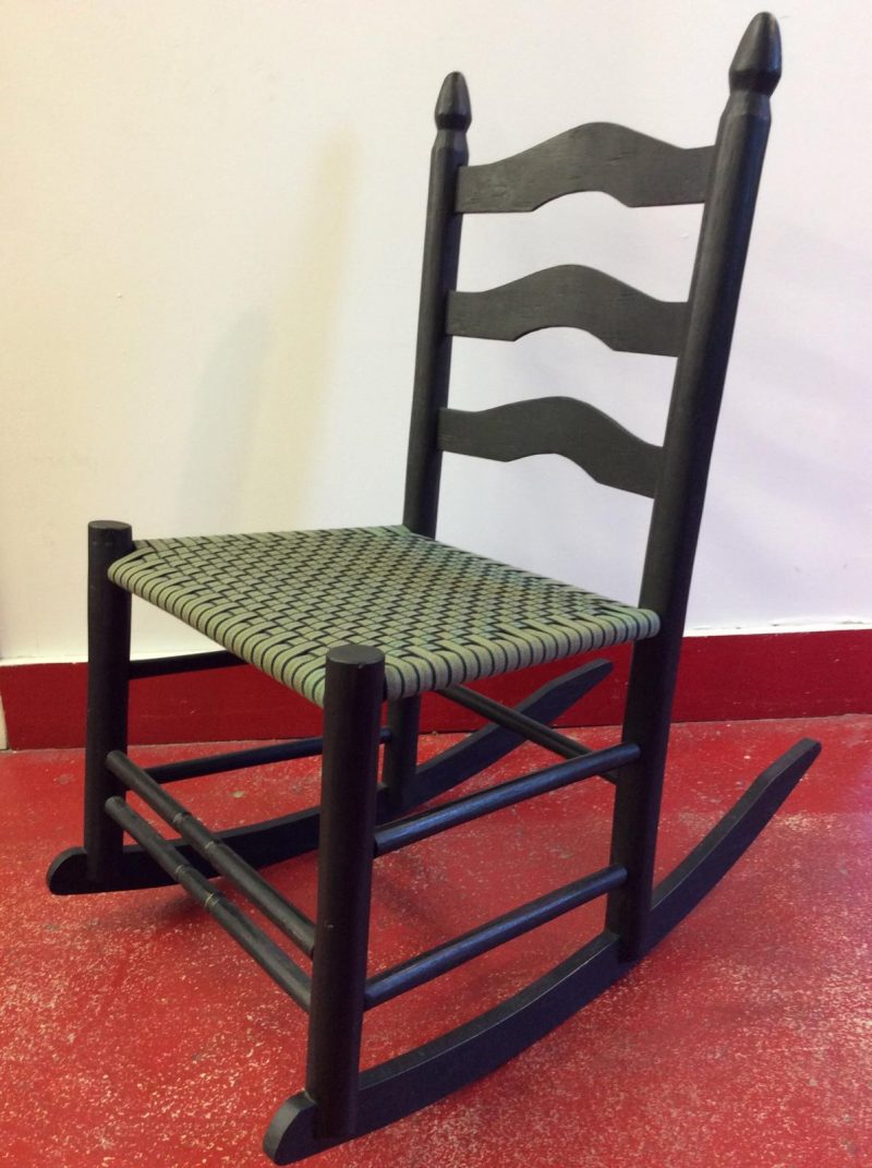 A black ladderback rocking chair with olive drab cotton tape woven seat