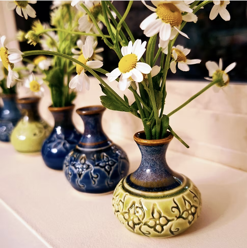 Tiny blue and green bud vases with daisies in them