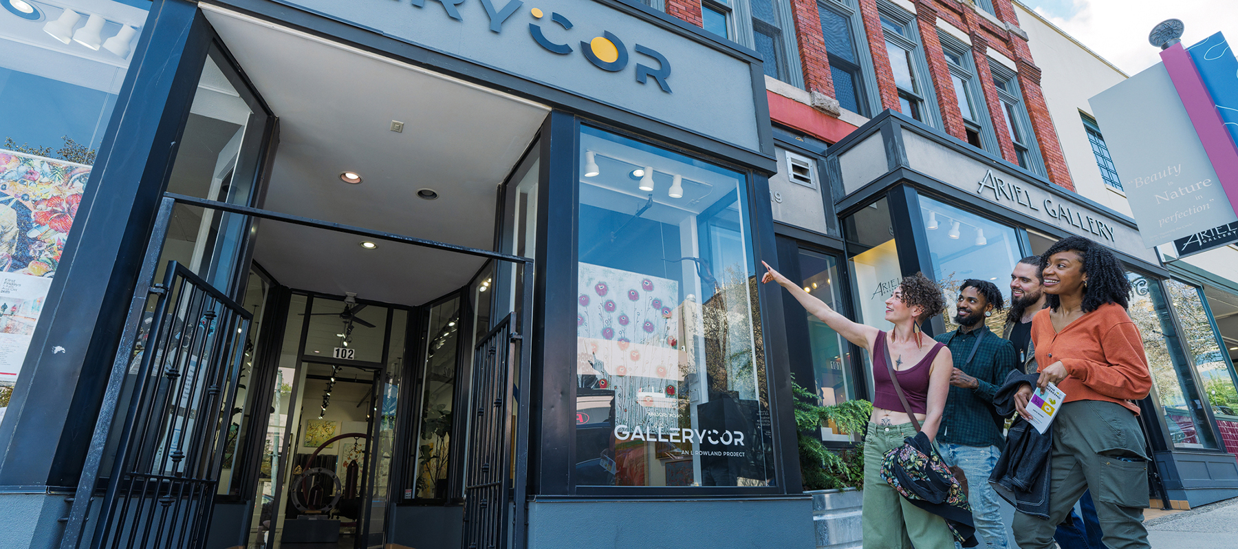 Group of diverse friends walking past a brick art gallery storefront with large glass windows and a blue-gray sign.